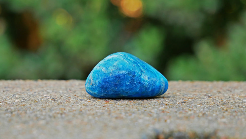 Up close of a tumbled apatite stone on pavement.
