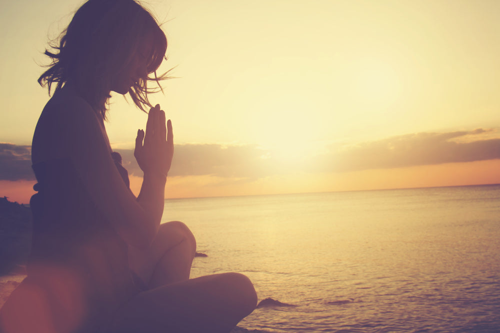 Woman doing yoga on the beach during a sunrise.